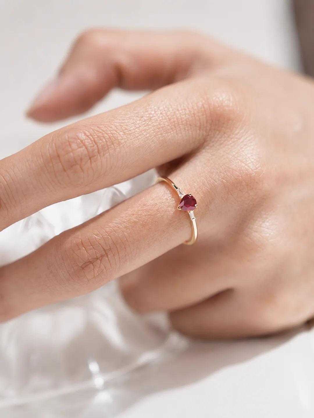 Gold ring with a red gemstone on a person's finger against a white background