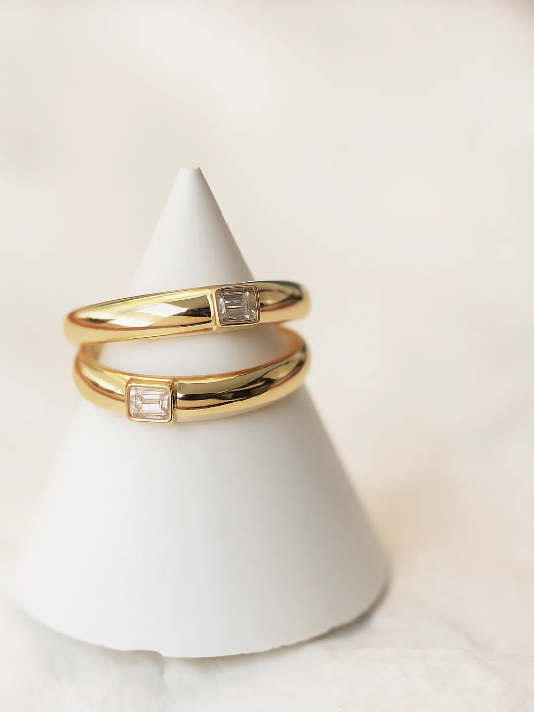 Two gold rings with embedded diamonds on a white cone-shaped stand by PETRALO